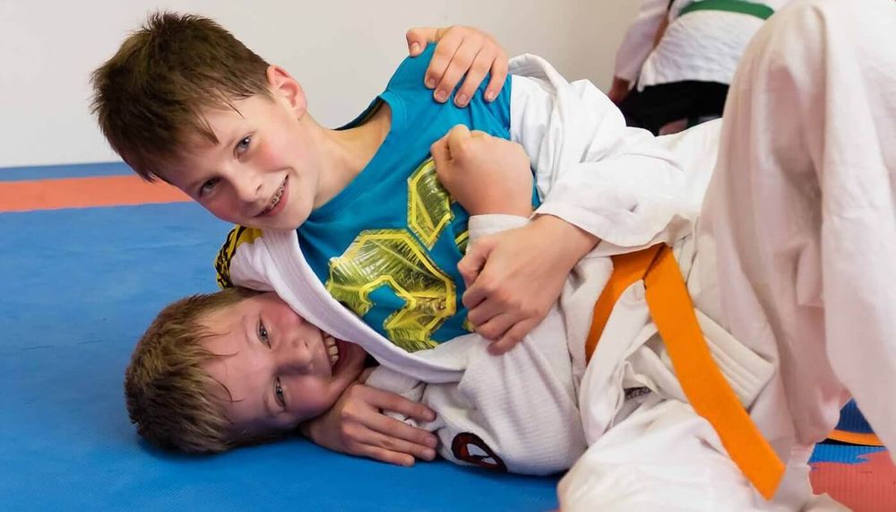 Zwei Jungen lachen beim Bodenkampf im Kindertraining